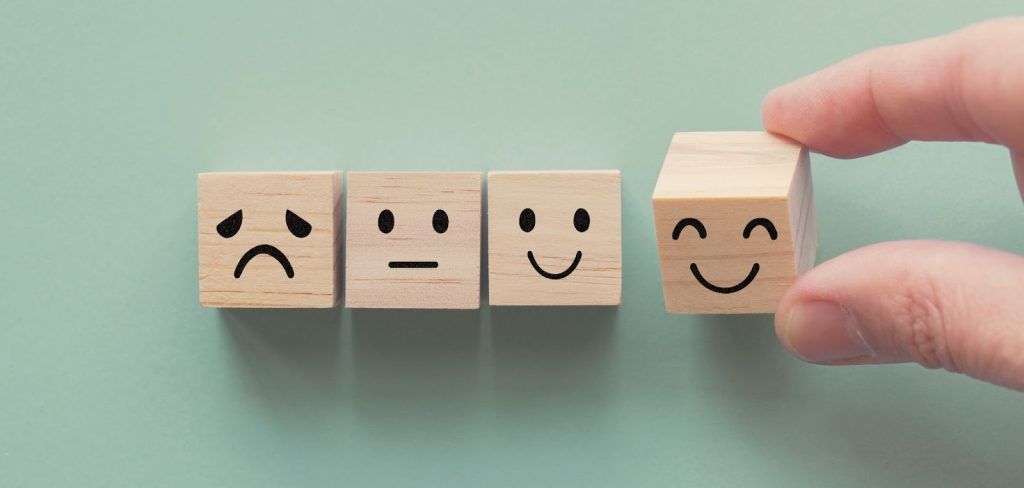Wooden blocks showing a progression of faces from sad to happy, with a hand placing the final smiling block.