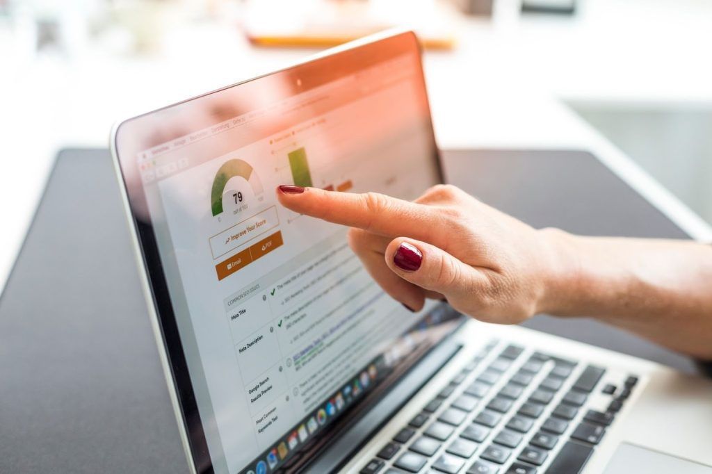 A close-up of a person's hand pointing at an SEO audit score of 79 on a laptop screen, displaying common SEO issues and optimization data.