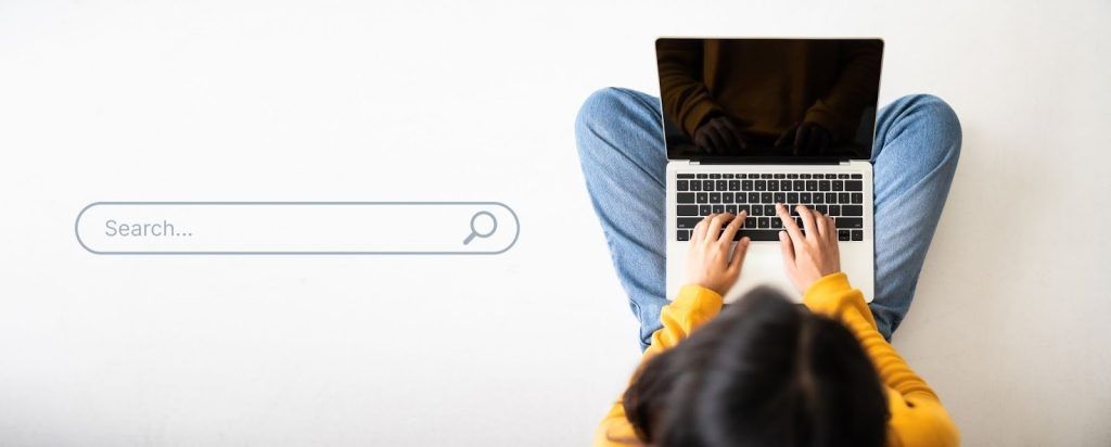 An overhead view of a person sitting cross-legged and typing on a laptop, positioned next to a digital 