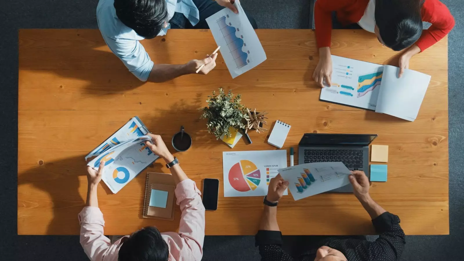 Overhead view of a team collaborating around a wooden table, analyzing charts and graphs, discussing data insights, and planning business strategies.