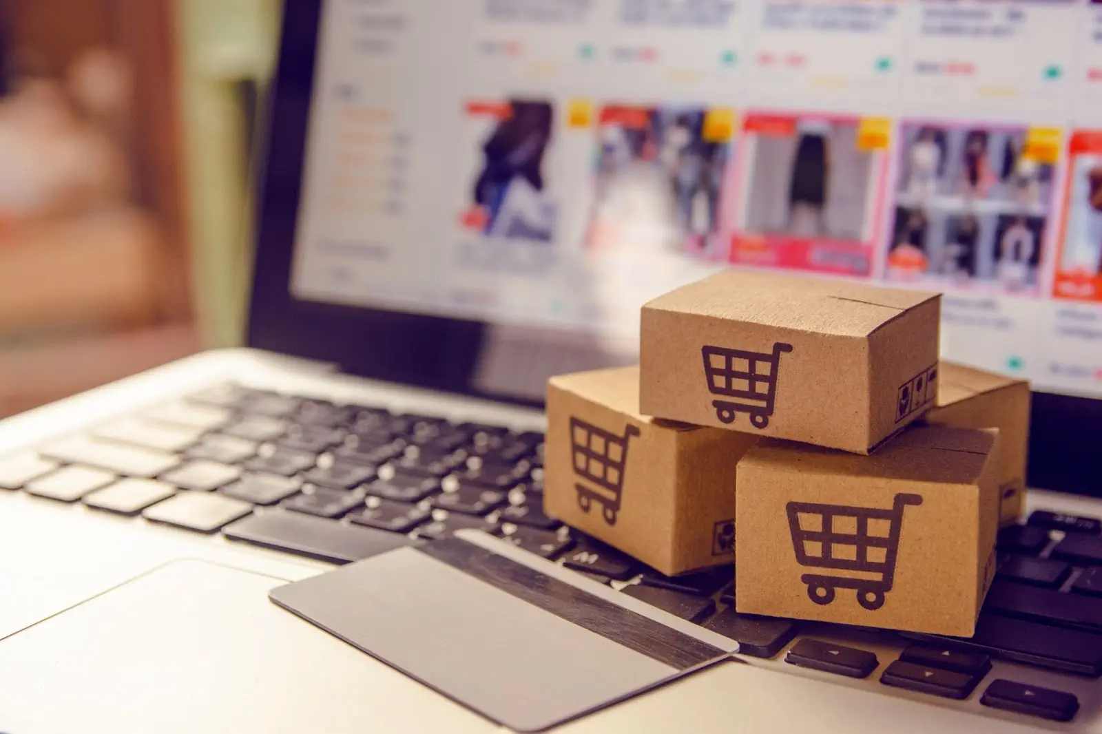 Laptop displaying an online shopping site with stacked boxes featuring shopping cart icons and a credit card.