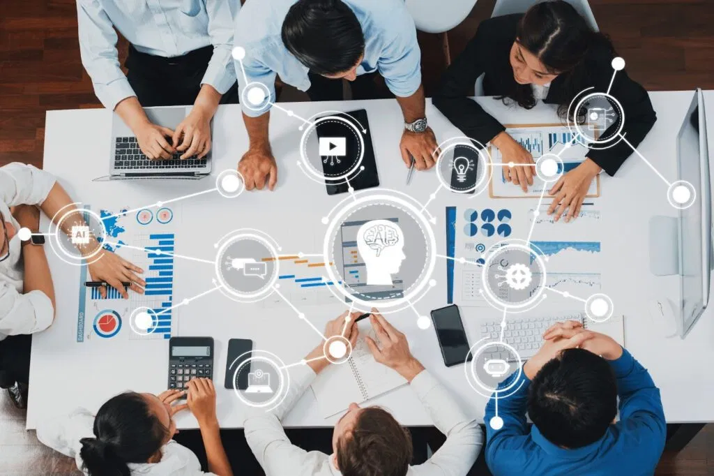 A team working at a table with laptops, charts, and digital icons representing AI and data analysis.